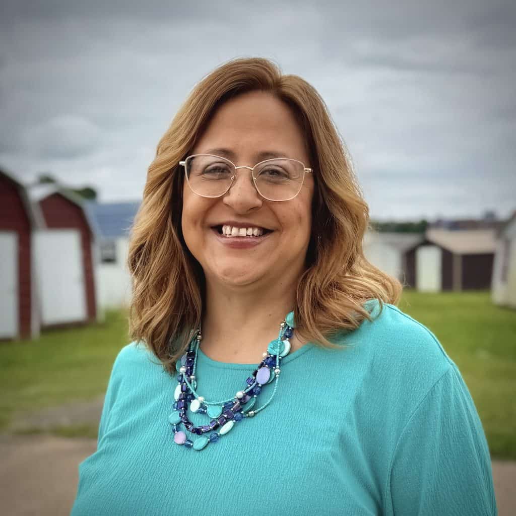 Smiling woman with glasses and necklace outdoors, representing GEMCO Buildings, Inc. team member.